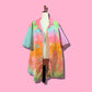 A short-sleeve button-up shirt with a vibrant pastel rainbow gradient and star and leaf patterns, displayed on a cream dress form mannequin against a solid pink background.