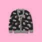 A cute opossum cardigan sweater with a black base and with a gray, white, and pink opossum pattern on a pink background.