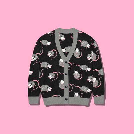 A cute opossum cardigan sweater with a black base and with a gray, white, and pink opossum pattern on a pink background.